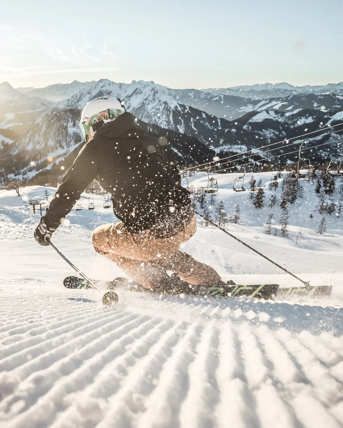 © Moritz Ablinger / Oberösterreich Tourismus GmbH Skifahrer zieht im Gegenlicht der tiefen Sonne seine Spur über eine frisch präparierte Piste, dahinter verschneite Berge