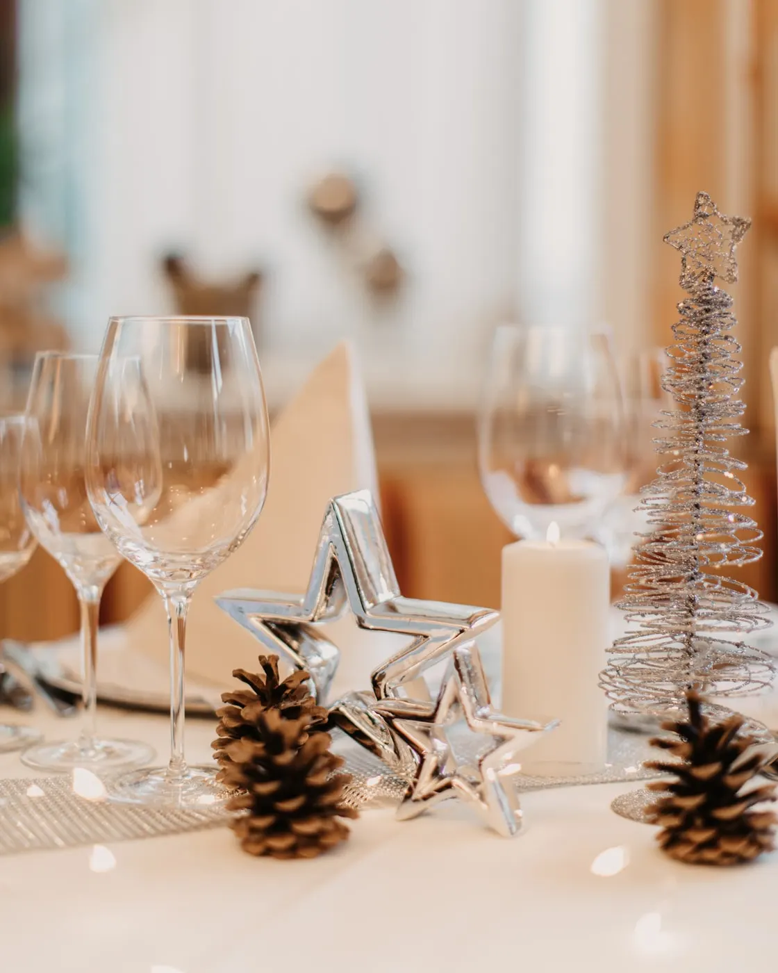 © Selina Flasch Photography Festlich gedeckter Tisch mit Weingläsern, silbernen Sternen, Tannenzapfen, einer brennenden Kerze und einem Bäumchen aus Silberdraht