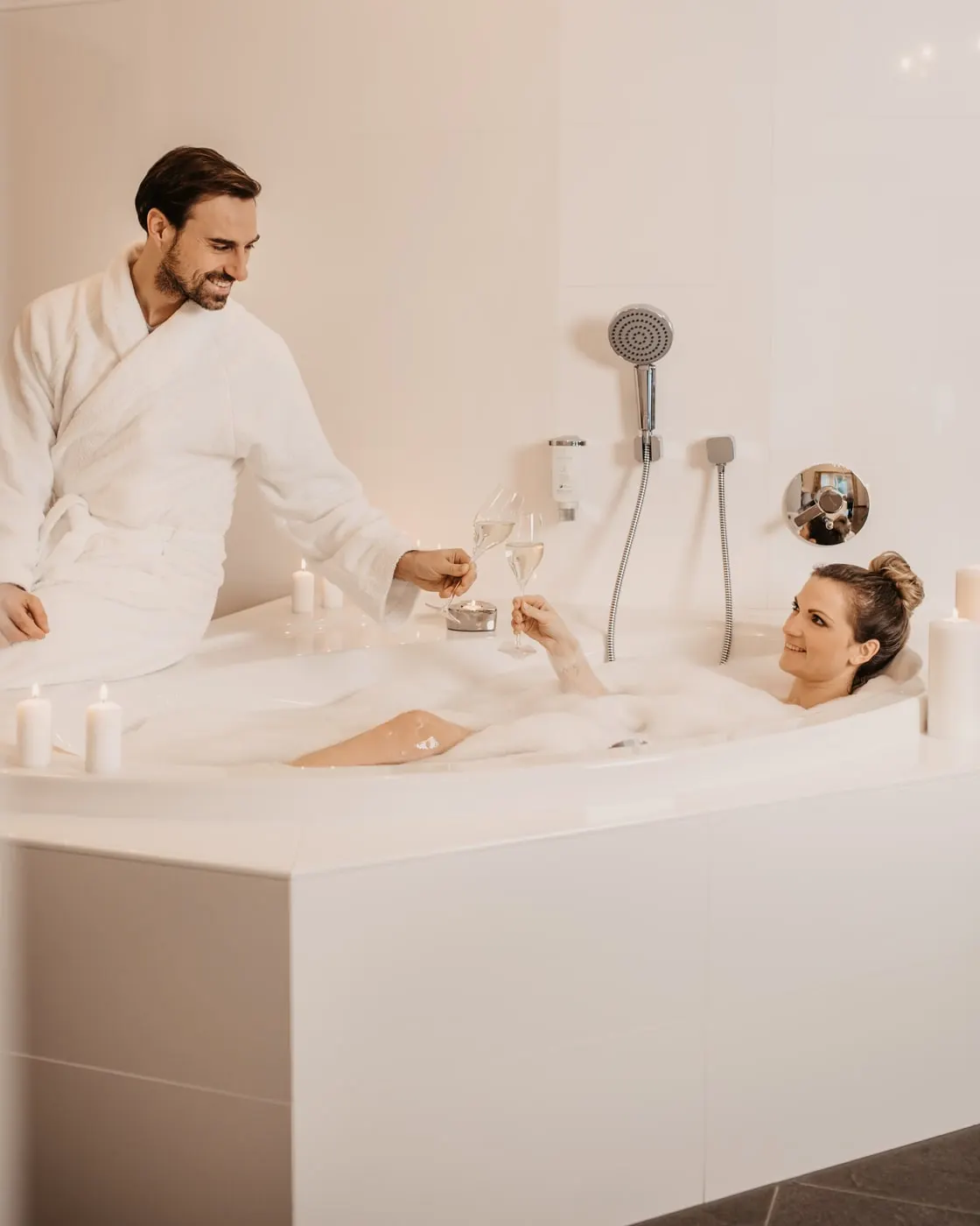 © Selina Flasch Photography Zwei Gäste stoßen bei Kerzenlicht mit Sekt an, sie im Schaumbad, er im Bademantel auf dem Wannenrand