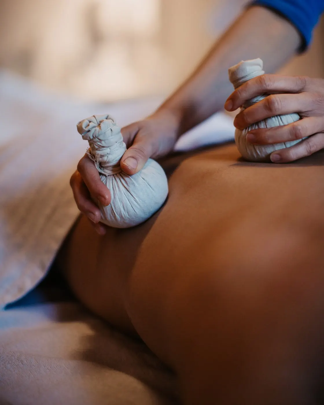 © Selina Flasch Photography Nahaufnahme einer Kräuterstempelmassage: Eine Hand drückt einen Kräuterstempel auf einen bloßen Rücken